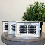 Eyelash extensions in clear cases on a wooden stool with a plant in the background